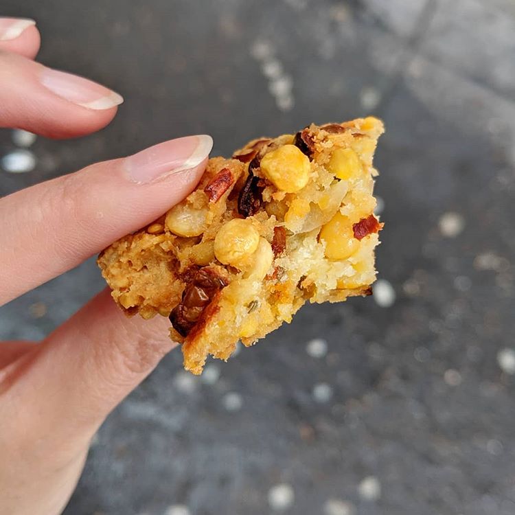 A piece of vadai held in a person’s hand.  Pieces of chana dal and dried chilli are visible.